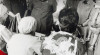 Foto kunjungan Presiden Soeharto di salah satu Posyandu di Jawa Barat pada10 Juni 1987. Presiden Soeharto didampingi oleh Menkokesra Alamsyah Ratu Perwiranegara, Ketua BKKBN Haryono Suyono, dan Gubernur Jawa Barat Yogi S. Memet.